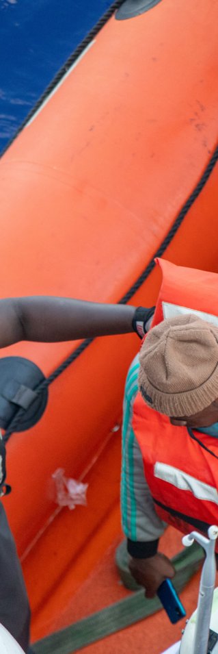 En man iklädd Läkare Utan Gränsers t-shirt hjälper en person av en gummibåt.