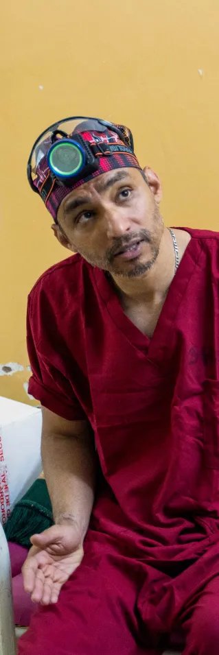 en man i operationskläder och en pannlampa diskuterar med kollegor på ett sjukhus i Khartoum