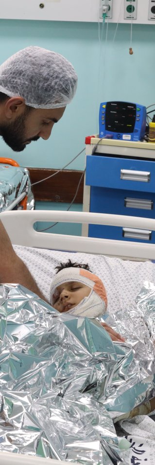 Medicinsk personal vid en sjukhussäng med en pojke med bandage runt huvudet