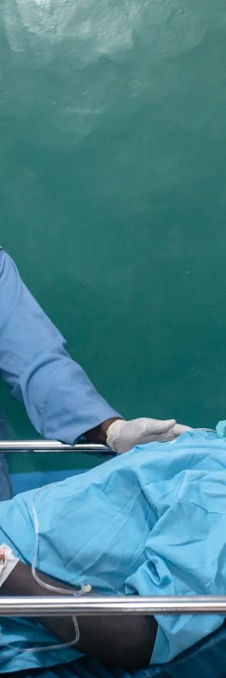 En sjuksköterska i operationskläder tar hand om en patient i en sjukhussäng