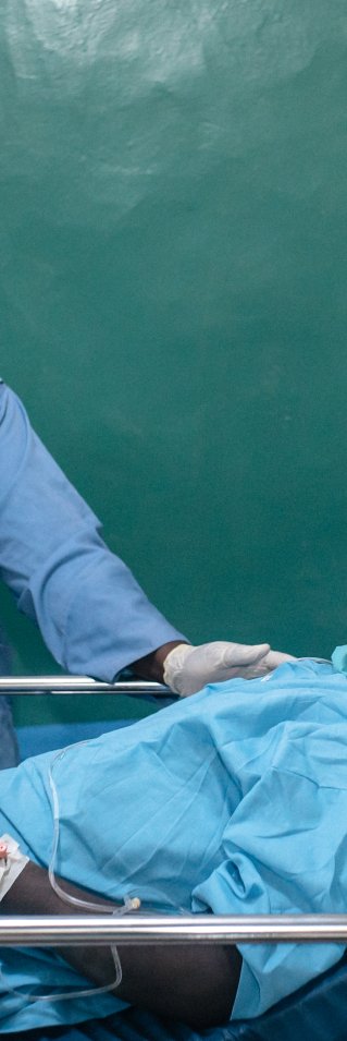 En sjuksköterska i operationskläder tar hand om en patient i en sjukhussäng