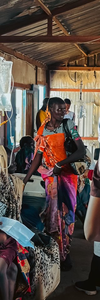 Ryggtavla av MSF-anställd omringad av patienter på en klinik.
