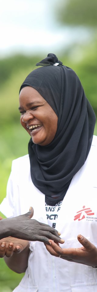 En kvinna i Läkare Utan Gränser väst och slöja skrattar tillsammans med två MSF volontärer.