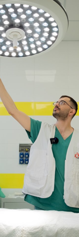 En sjukvårdsanställd med Läkare utan gränser-väst sträcker sig upp mot en lampa i en sjukhussal.