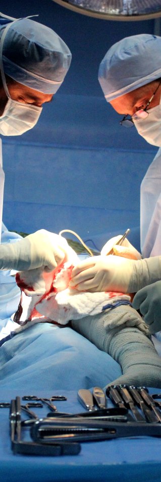 Tre kirurger utför en operation på en patients ben.