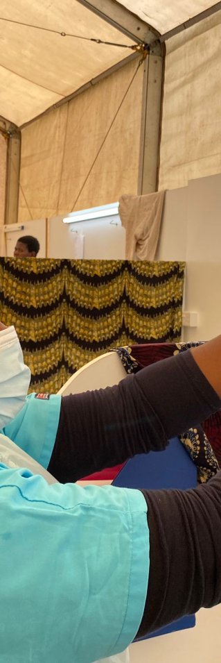 En kvinna i gröna sjukhuskläder och munskydd fixar till en påse dropp.