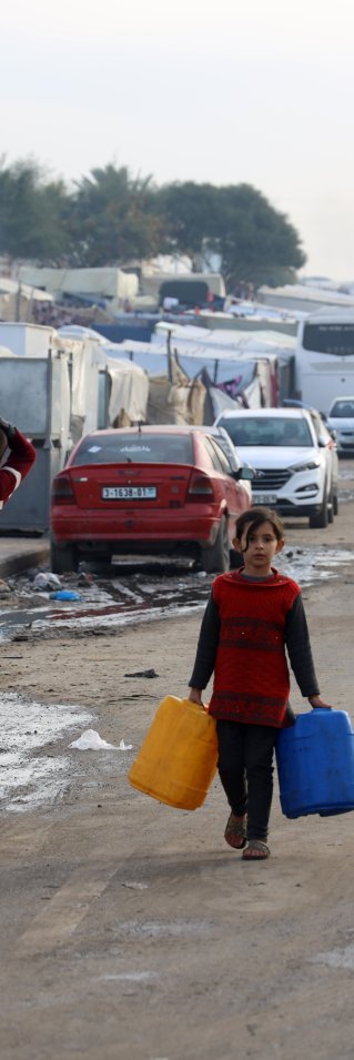 Flera människor bärandes på vattendunkar går längs en gata södra i Gaza.