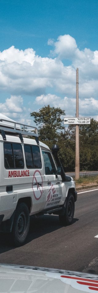 En ambulans med en flagga med Läkare Utan Gränsers logga på en rak asfalterad väg. 