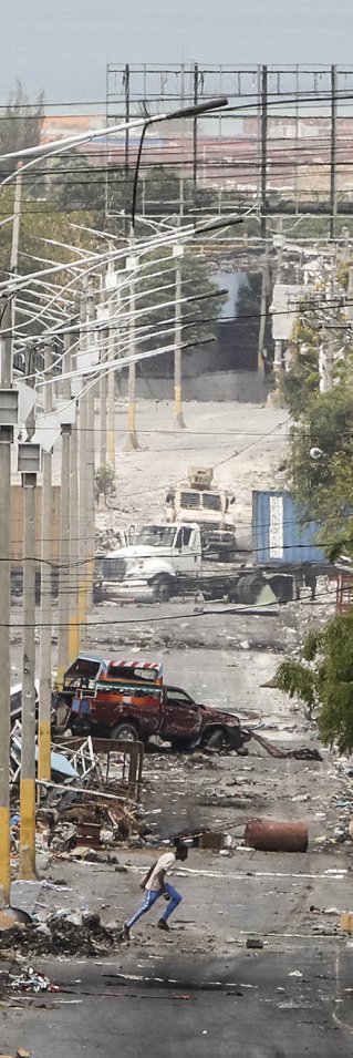 Man i urban miljö med utbrunna bilvrak och uppriven asfalt