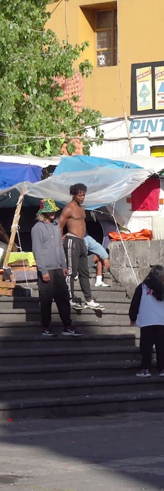 Tältläger i urban miljö. Två personer i Läkare Utan Gränser-västar pratar med en grupp migranter