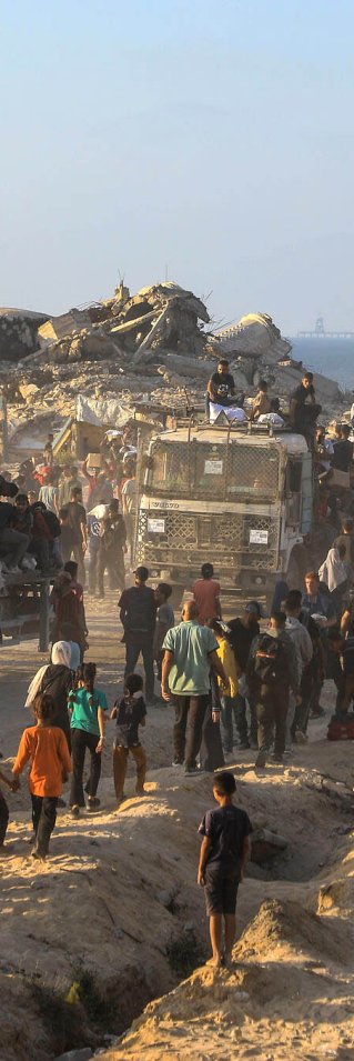 En lastbilskonvoj med förnödenheter möts av en stor mängd människor bland runier med havet som fond