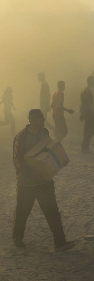 Folksamling i motljus. Man i förgrunden bär en kartong.