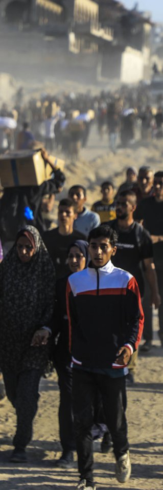 Människor i en stor folkmassa rör sig längs en dammig väg, flera bär kartonger