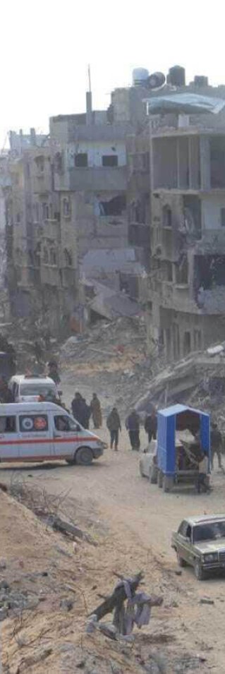 En ambulans parkerad på en väg i ett ruinlandskap. Grupper av människor rör sig längs vägen