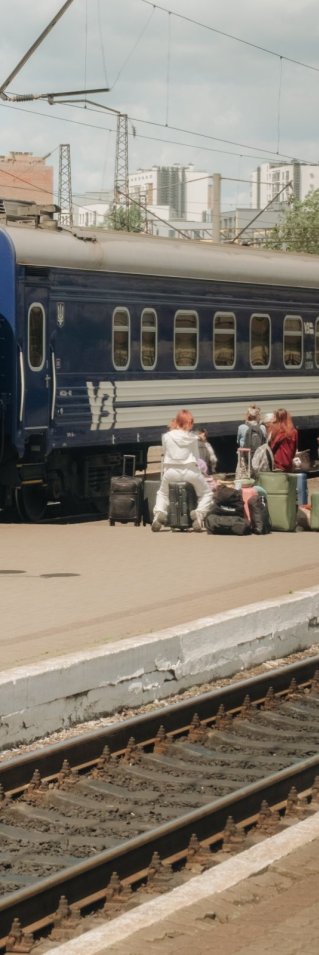 Tågräls och ett tåg med människor som väntar med väskor på perrongen.