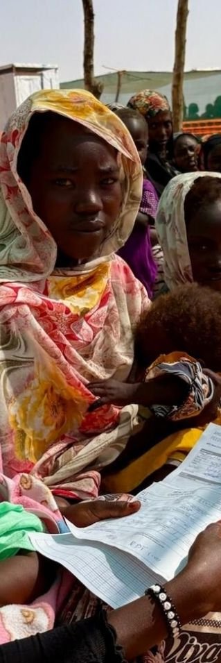 Kvinnor och barn sitter i skugga utanför klinik