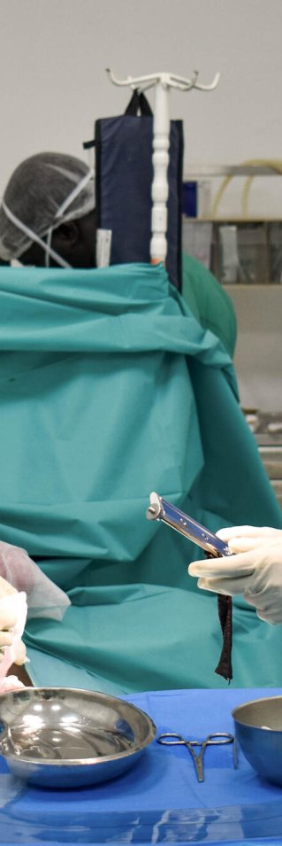 Två kirurger i heltäckande sjukhusdräkter, munskydd och handskar vid ett bord med sjukvårdsutrustning.
