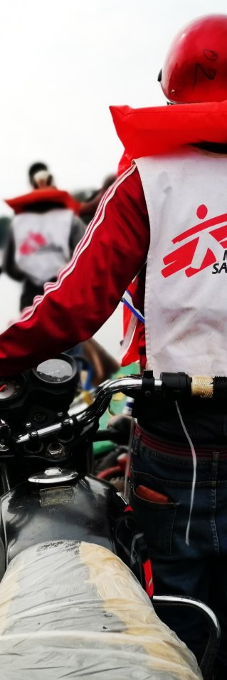 Två personer transporterar motorcyklar i en kanot över floden.