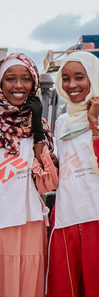 Två kvinnor i msf-västar framför en jeep