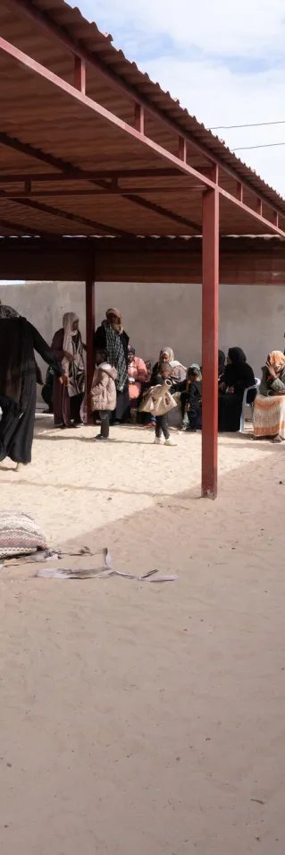 Människor sitter i skuggan på stolar längst en vägg på en innergård