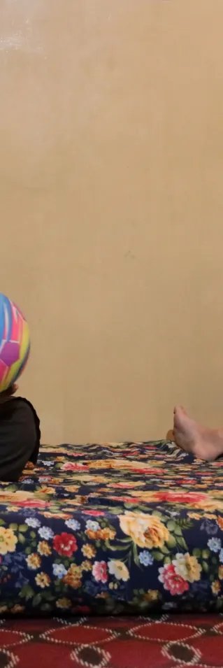 En man och ett barn sitter på en madrass. Mannen håller i en boll och barnet ler.