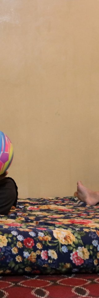 En man och ett barn sitter på en madrass. Mannen håller i en boll och barnet ler.