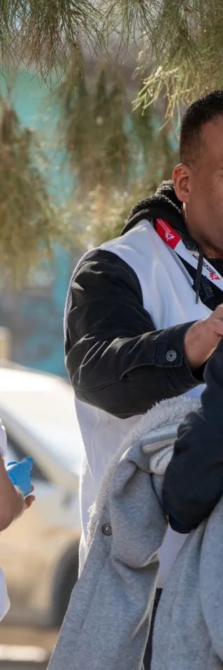 Två personer i vit Läkare Utan Gränser-väst. En av personerna lägger handen på axeln på en tredje person i svart huvtröja.