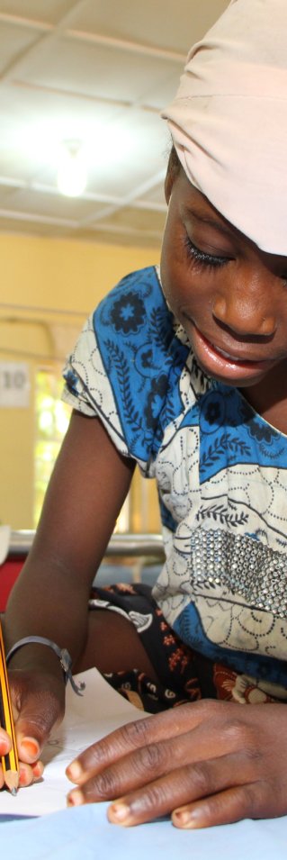 Flicka med sjukdomen noma efter operation sitter i en säng och ritar