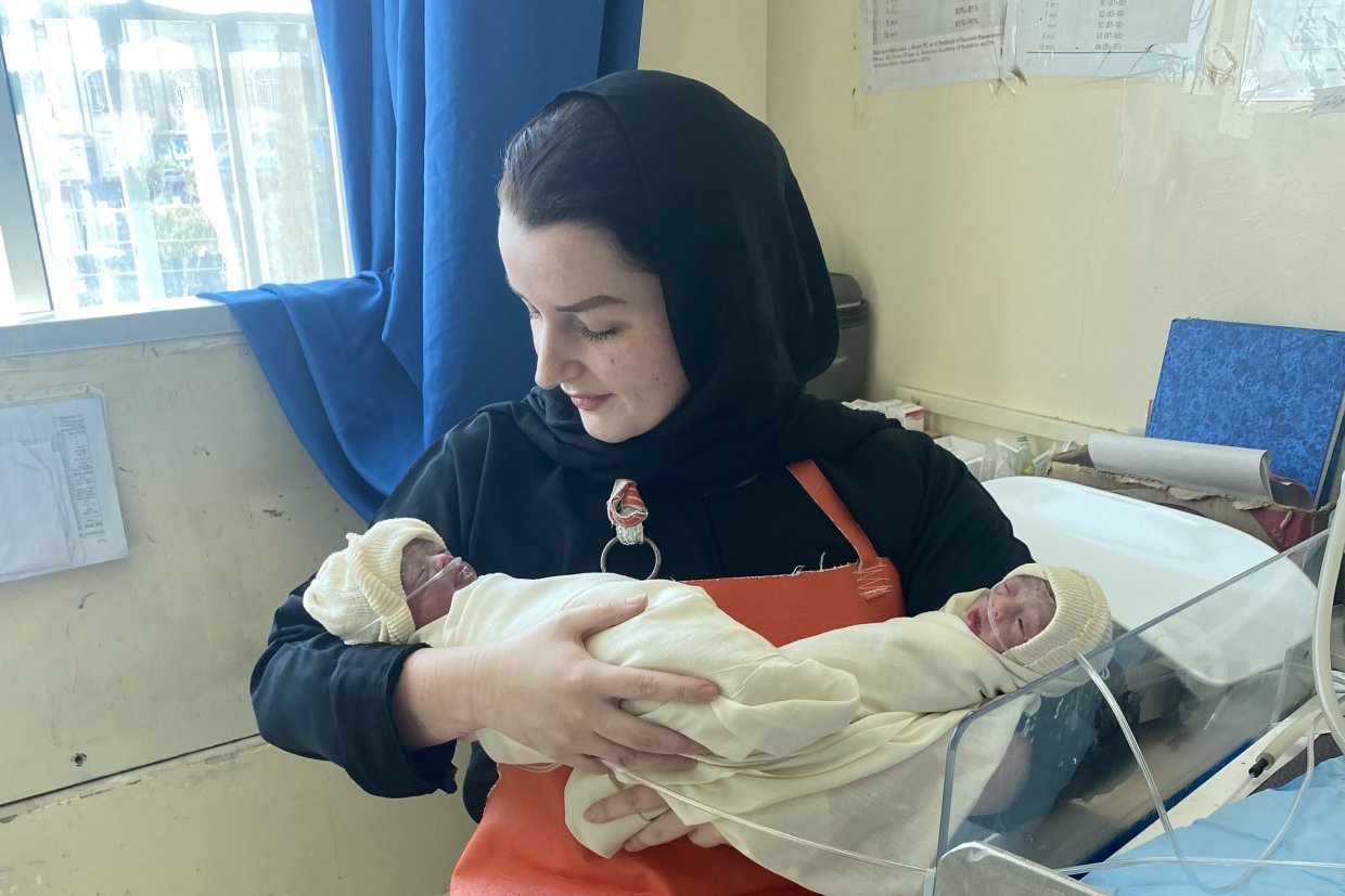 En kvinna håller i två nyfödda barn insvepta i filtar