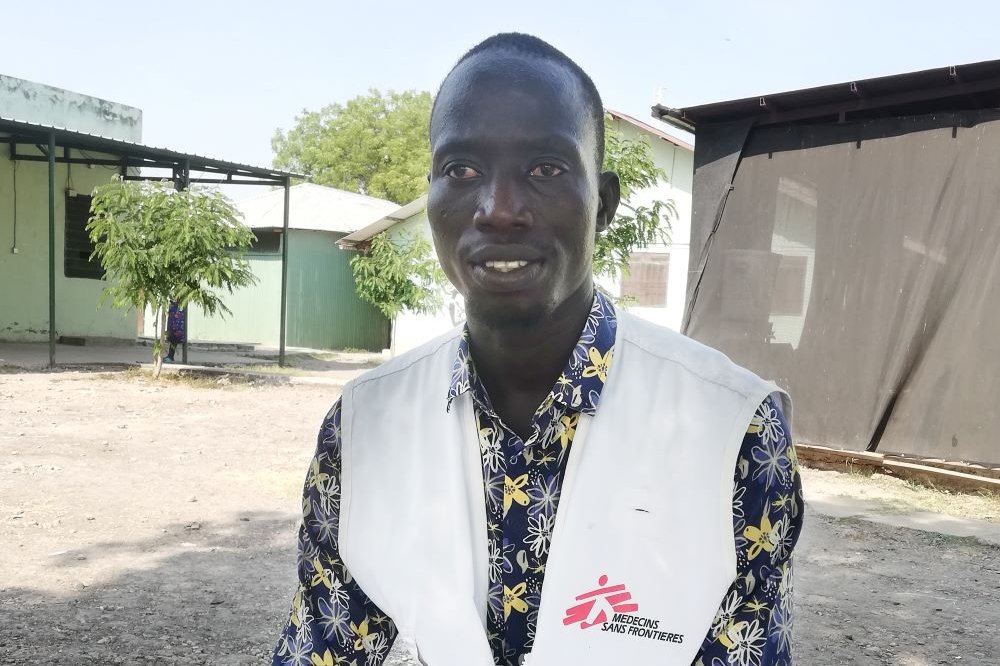 En man med Läkare Utan Gränser-väst sitter ner. Byggnader i bakgrunden.