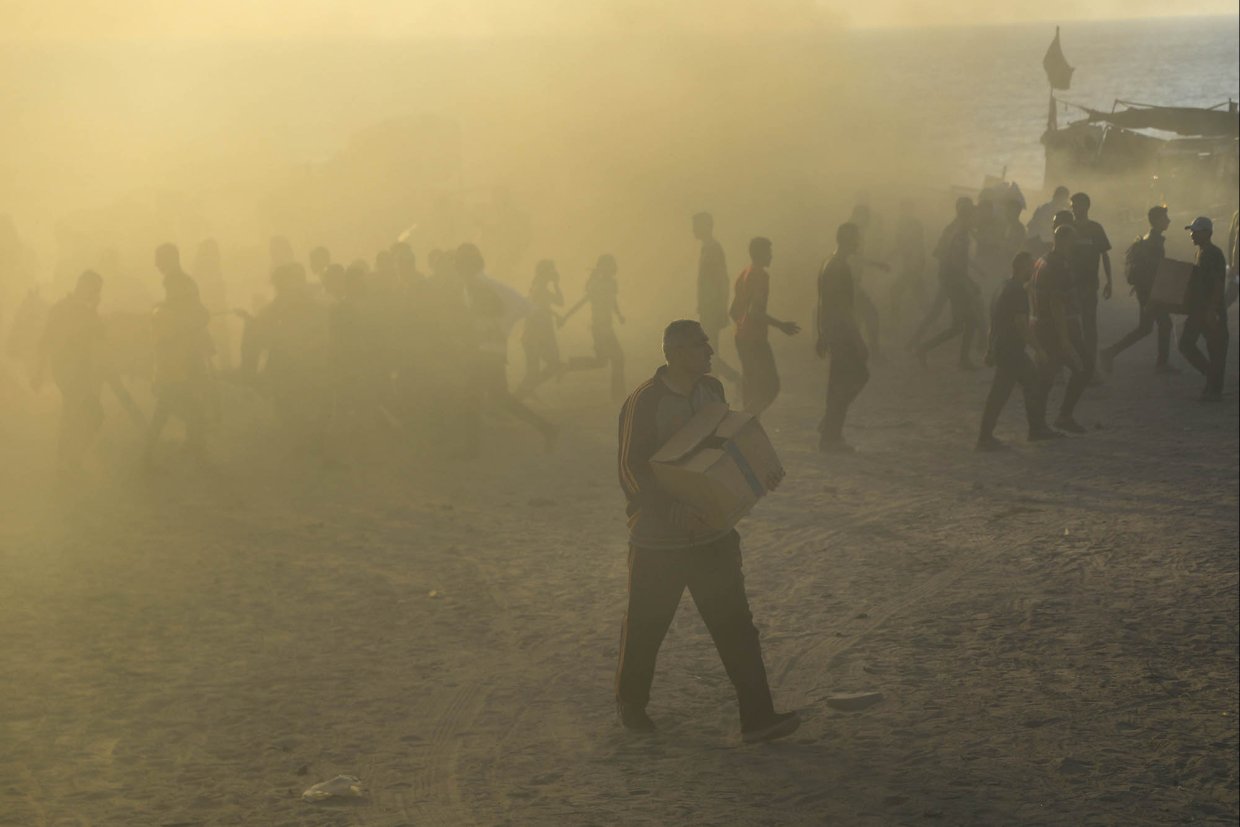 Folksamling i motljus. Man i förgrunden bär en kartong.