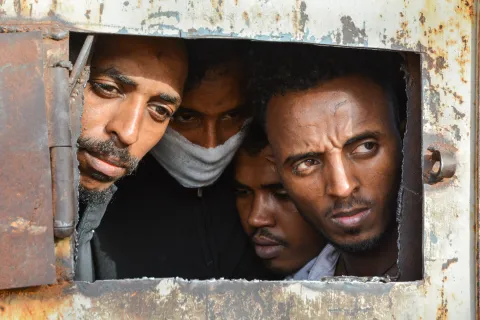 Fyra män tittar ut från ett förvar i Libyen.