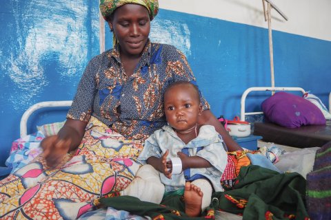 En kvinna sitter på en säng och håller om en liten pojke.