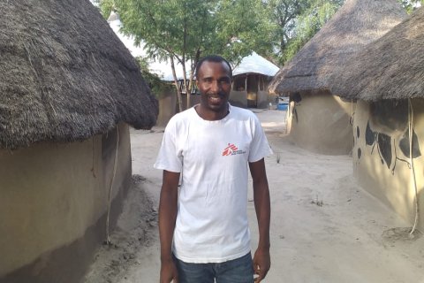 En man står framför några hus i Sydsudan och tittar in i kameran.