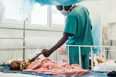 Tvååriga Sheku Kamara, som ligger på sängen på Läkare Utan Gränsers sjukhus i Kenema, Sierra Leone, håller en anställd i handen.