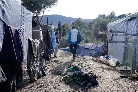 En anställd från Läkare Utan Gränser går, med ryggen mot kameran, på en grusväg genom ett läger på den grekiska ön Samos.