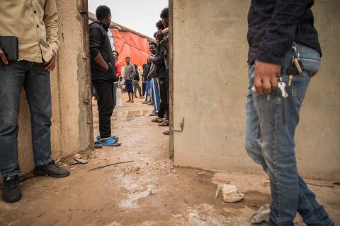 Människor står vid en dörröppning i förvaret Dahr-el-Jebel i Libyen. Det är lerigt på marken.