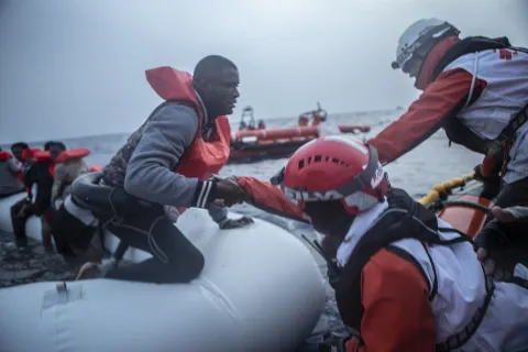 En man får hjälp av Läkare Utan Gränsers medarbetare att ta sig från en vattenfylld gummibåt till vår båt som ingår i vår sök- och räddningsinsats på centrala Medelhavet.