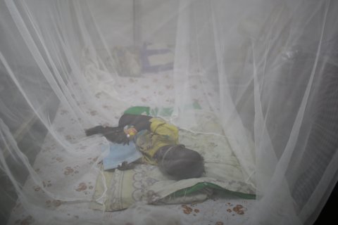Ett barn ligger under ett myggnät på en säng i Sydsudan.