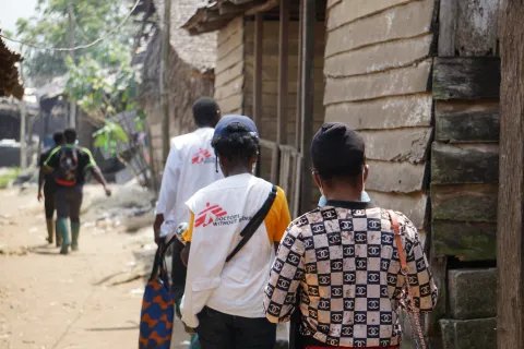 Tre medarbetare går längs en sandig väg mot byn Enyenge i Kamerun.
