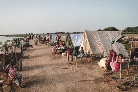 Människor sitter i tillfälliga skydd byggda på en väg i översvämningsdrabbade Pakistan.