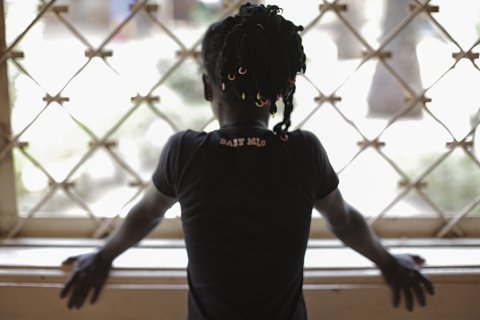 Ung kvinna står med ryggen vänd mot kameran och tittar ut genom ett fönster