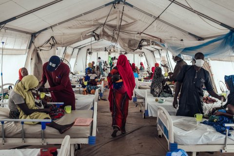 Inuti ett stort tält ligger ett tjugotal personer på sängar, både vuxna och barn.