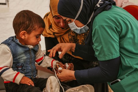 Två kvinnor står vid ett litet barn och kollar på hans hand. 