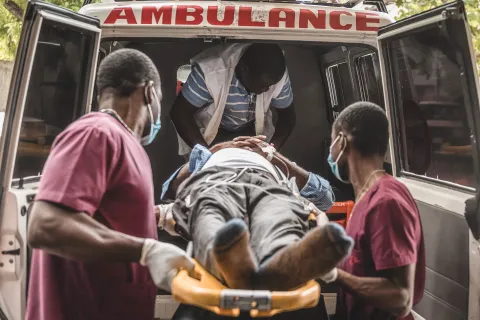 Två sjukhusklädda män bär in en person liggandes på en bår in i en ambulans