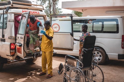 En gravid kvinna hjälps ut från en ambulans utav en person i sjukhuskläder.