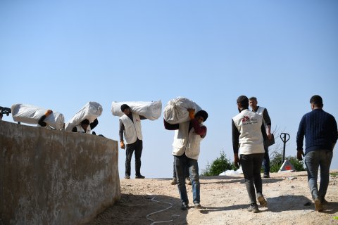 Flera män i Läkare Utan Gränser västar bär påsar med tält över sina axlar.
