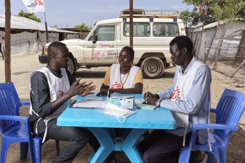 Tre personer i Läkare Utan Gränser västar sitter runt ett bord och diskuterar.