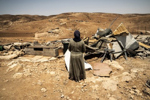 Framför några ruiner står en kvinna med ryggen mot kameran.