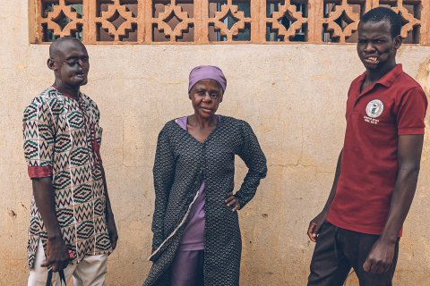 Två män och en kvinna som överlevt noma står med ryggen mot en vägg.